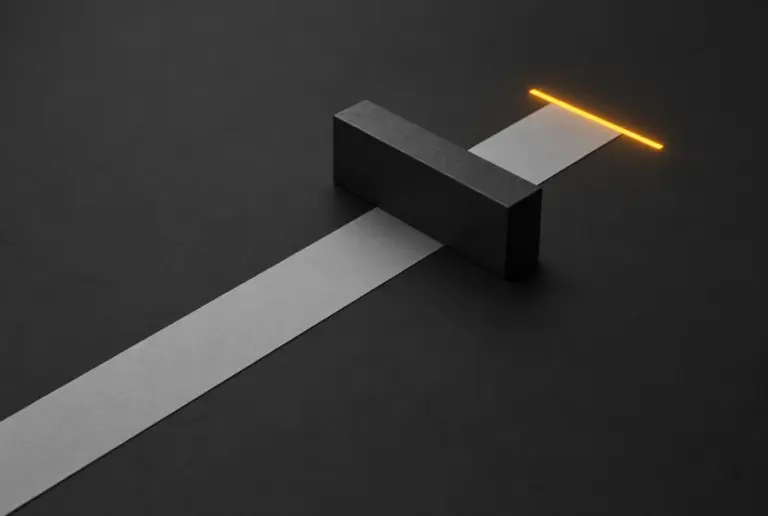 A strip of paper passing under a heavy black barrier block